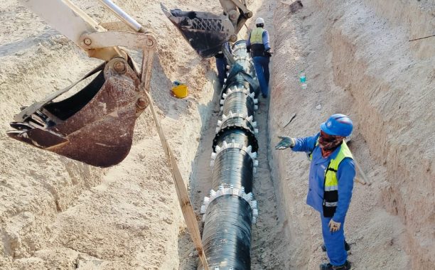 Two workers are installing concrete drains on the side of the road, which is a large power plant construction. Backhoe lifting of concrete pipe drainage system.